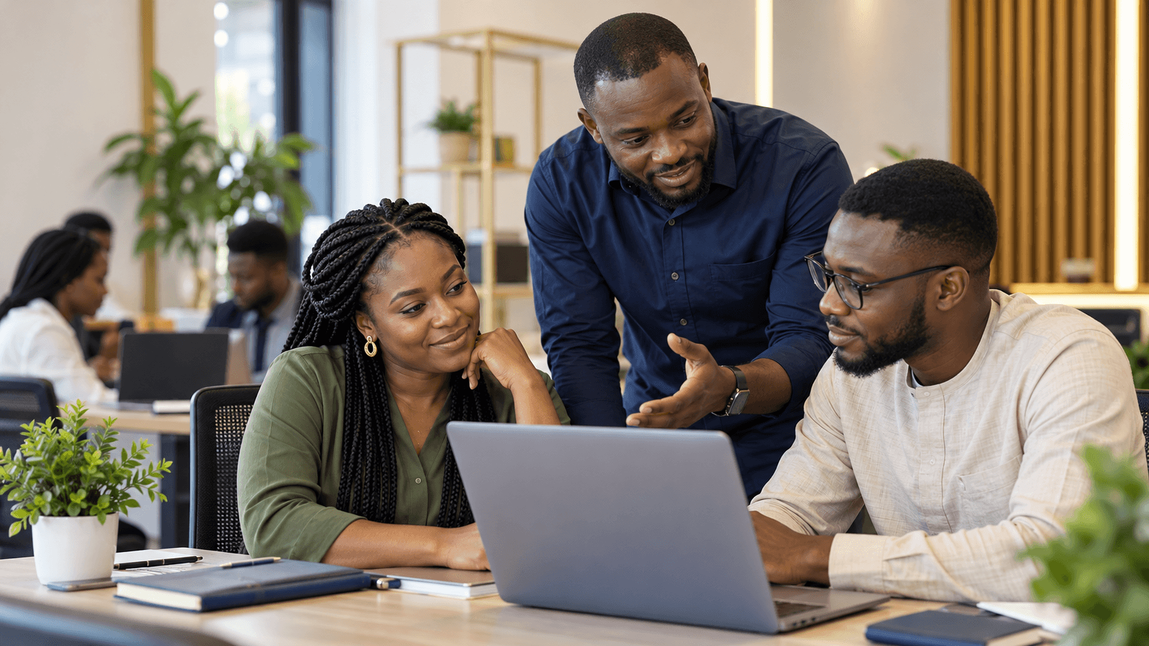 An instructor leans in to guide two learners working together on a laptop.